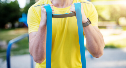 Man working out with resistance rubber bands in street, close up