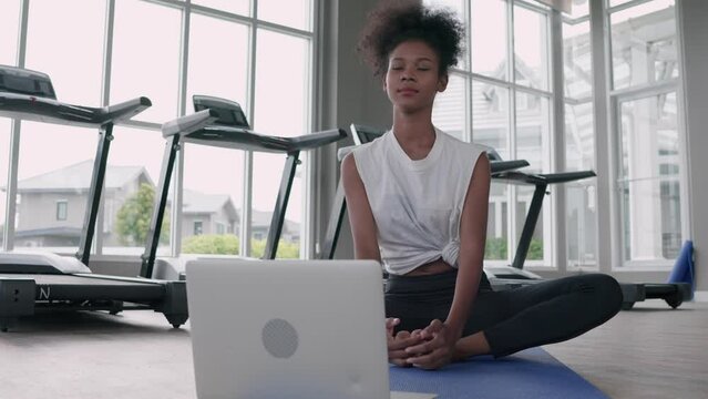 Attractive, Fitness young black woman doing exercise yoga in gym. African american female loook at laptop lesson practicing Yaga lotus pose on social online internet class. Healthy lifestyle concept.