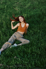 A woman lies on fresh spring green grass in a park without mosquitoes or ticks and enjoys relaxing while watching the sunset. The concept of safe outdoor recreation