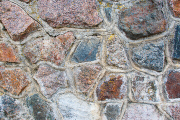 A close-up of the stone wall. The texture of masonry is made of multi-colored stones connected with cement mortar.