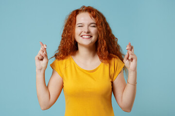 Young worried fun redhead woman in yellow t-shirt waiting for special moment, keeping fingers...