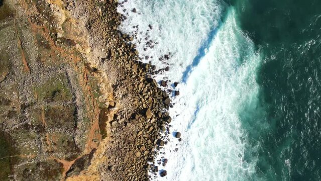 Aerial view of rocky beach with waves and clear ocean water. Drone top view