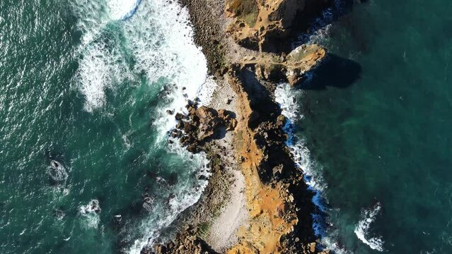 Aerial view of rocky beach with waves and clear ocean water. Drone top view