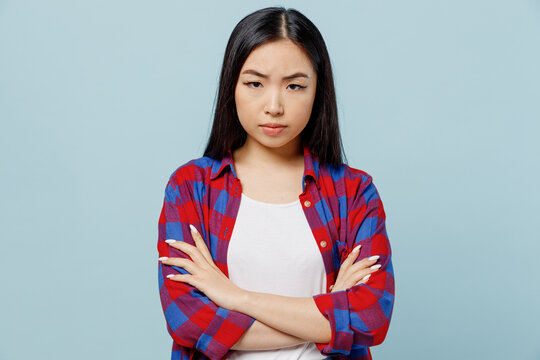 Young sad dissatisfied displeased strict woman of Asian ethnicity 20s wearing checkered shirt hold hands crossed folded isolated on plain pastel light blue color background. People lifestyle concept.