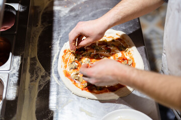 Pizza making process. Male chef hands making authentic pizza in the pizzeria kitchen.
