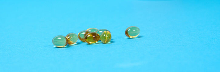 Capsules of vitamin D on a blue background, a long banner with space for text. Vitamins for people