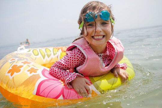 Girl on a swim ring in the ocean smiling with googles on her head