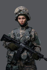 Studio shot of isolated on gray background woman soldier holding rifle.