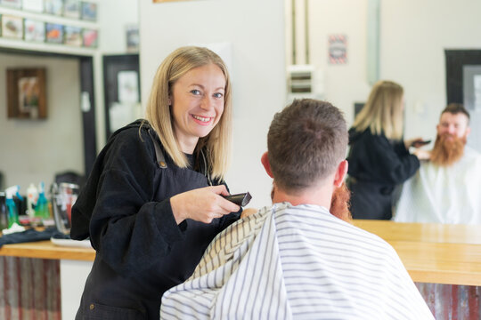 A smiling woman barber trimming hair off the back of a man's neck