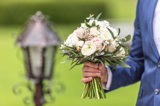Groom holds a wedding bouquet with white flowers outdoors on a wedding day