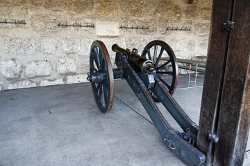shooting cannon with wheels from the middle ages in front of a white stone wall, object ideal for...