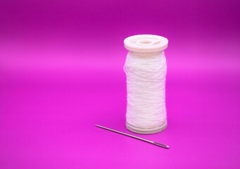 White thread spool with needle for sewing isolated on purple background