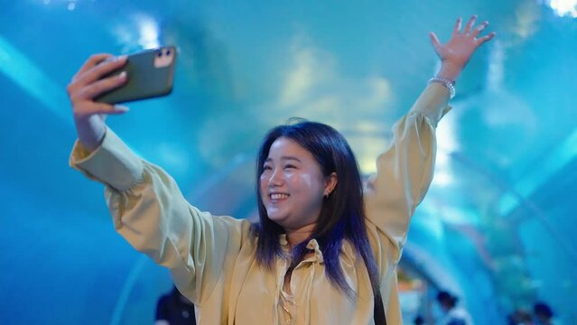 Asian woman taking selfie by smartphone at big aquarium fish.