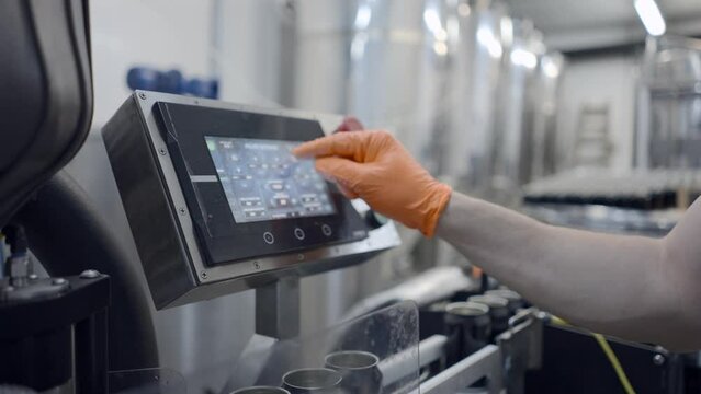 Worker's Hand In Rubber Glove Pressing On Automated Machine In A Beer Factory. Canning Beers. dolly-out shot