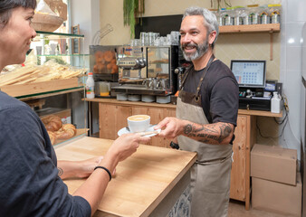 Smiling waiter serving a cup of coffee to the customer in the cafe