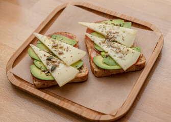 Vegetarian sandwich with avocado and tomato and cheese on a wooden board