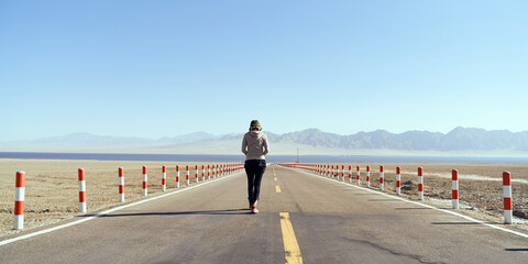 asian woman tourist walking towards a lake on empty open road
