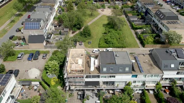 Aerial overview of wooden frame of roof structure under construction. Drone flying backwards and revealing a beautiful suburban neighborhood
