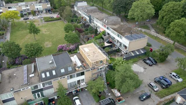 Aerial overview of wooden frame of roof structure under construction in a busy suburban neighborhood - Drone flying backwards