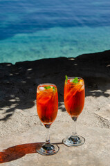 Two glasses of spritz long drink cocktail on stone with sea view background.