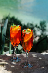 Two glasses of spritz long drink cocktail on stone with sea view background.