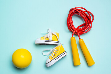 yellow sneakers, a red jump rope and a yellow ball lie on a blue background. sports and health