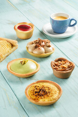 Six tartlets of different fillings on a wooden table, with a cup of coffee on the background