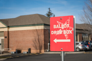 Bright red sign reading Ballot Drop Box at voting location. Selective focus with intentional...