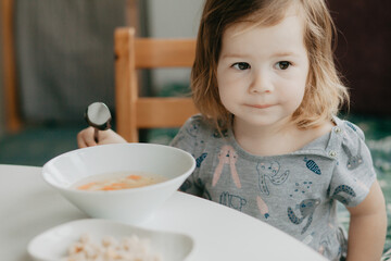 a little girl is sitting at the kitchen table eating soup