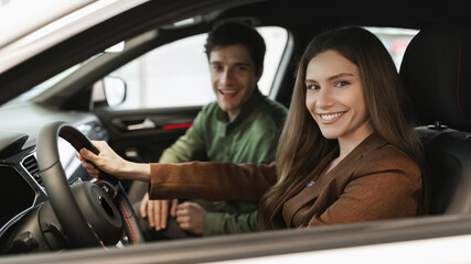 Cheery young couple sitting inside new car, checking it before purchase at dealership store, banner design