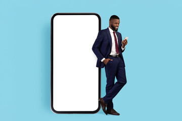 Business App. Black Businessman In Suit Standing Next To Big Blank Cellphone