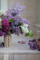 A large lush bouquet of lilacs of different varieties in a vase on a bright loggia. Calm rest at home with a glass of soda.