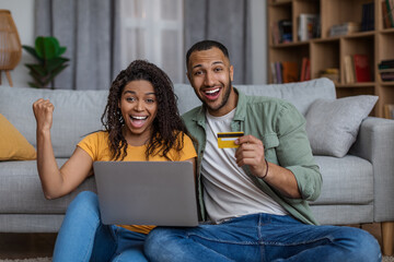 Excited african american couple with laptop and credit card celebrating success, emotionally reacting to online profit