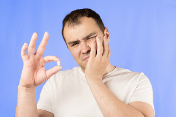 Man in a white T-shirt on a blue background holds a wisdom tooth in his hands after surgical tooth...