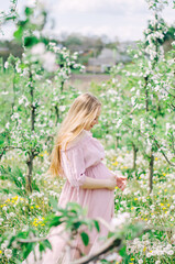 Pregnant girl in a pink dress in a flower garden with green trees and flowers