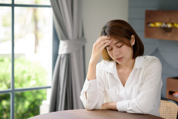 An Asian woman places her hands near her head while suffering from a headache.