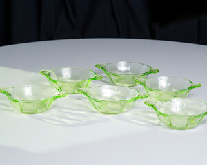 Set of 6 uranium depression glass glowing green with shadow on white table - Modern product shot