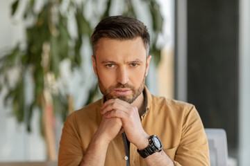 Serious Businessman Looking At Camera Sitting At Workplace In Office