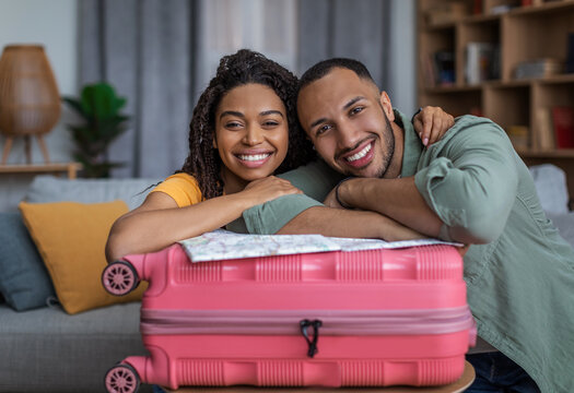 Positive african american couple leaning on suitcase and smiling at camera, ready for vacation abroad, free space
