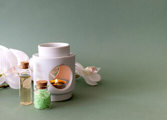 Sea salt for baths and body oil on a green table. A tea candle in a candlestick and a sprig of white orchid in the background. Light green background, place for text