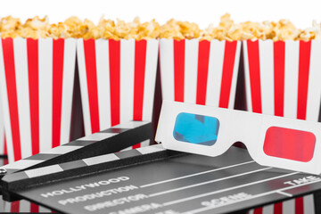 Cinema, movie, leisure and theater concept. Popcorn boxes with white and red stripes full of sweet with caramel popcorn, 3D glasses and clapperboard on black reflective background