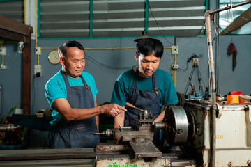 A skilled senior mechanic is teaching his son how to use steel turning tools, and teaching how to operate the machine closely, in a small family-owned factory.