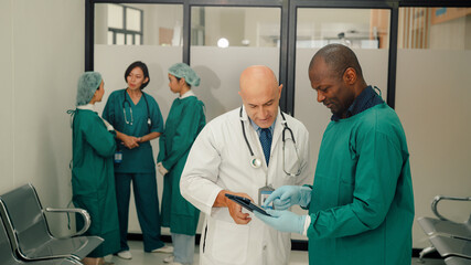 Male Surgeon and Doctor Consult Using Digital Tablet Computer while Talking about Patient's Health.