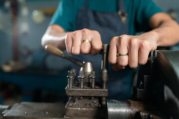 Close-up of a steel lathe with an iron insert, and iron is being machined in the machine, with mechanics closely operating the machine, in a small family-owned factory.