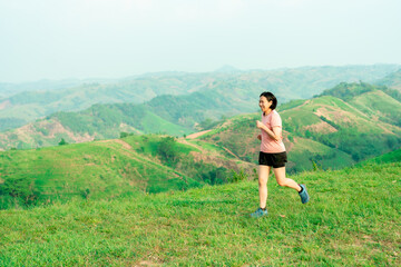 Obraz premium Young Asian woman runner, wearing black sportswear, running on a big mountain trail, cool morning, windmills, and sky in the background.