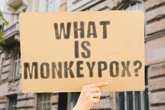 The question " What is monkeypox? " is on a banner in men's hands with blurred background. Diagnosis. Headache. Medical. Outbreak. Treatment. Swollen. Human. Pox. Disease. Epidemic. Virus. Health