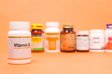 Vitamin D in a white jar with other dietary supplements on an orange background