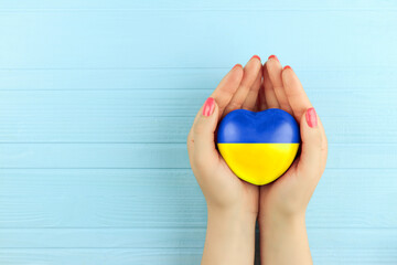female hands holding a painted heart in the Ukrainian flag