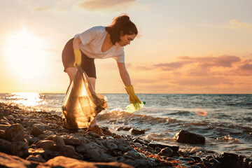 A female volunteer is collecting plastic garbage on the seashore. Cleaning of the coastal zone....