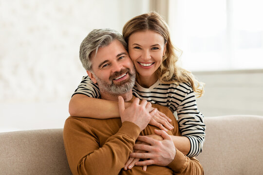 Loving Middle Aged Couple Embracing Sitting On Sofa At Home